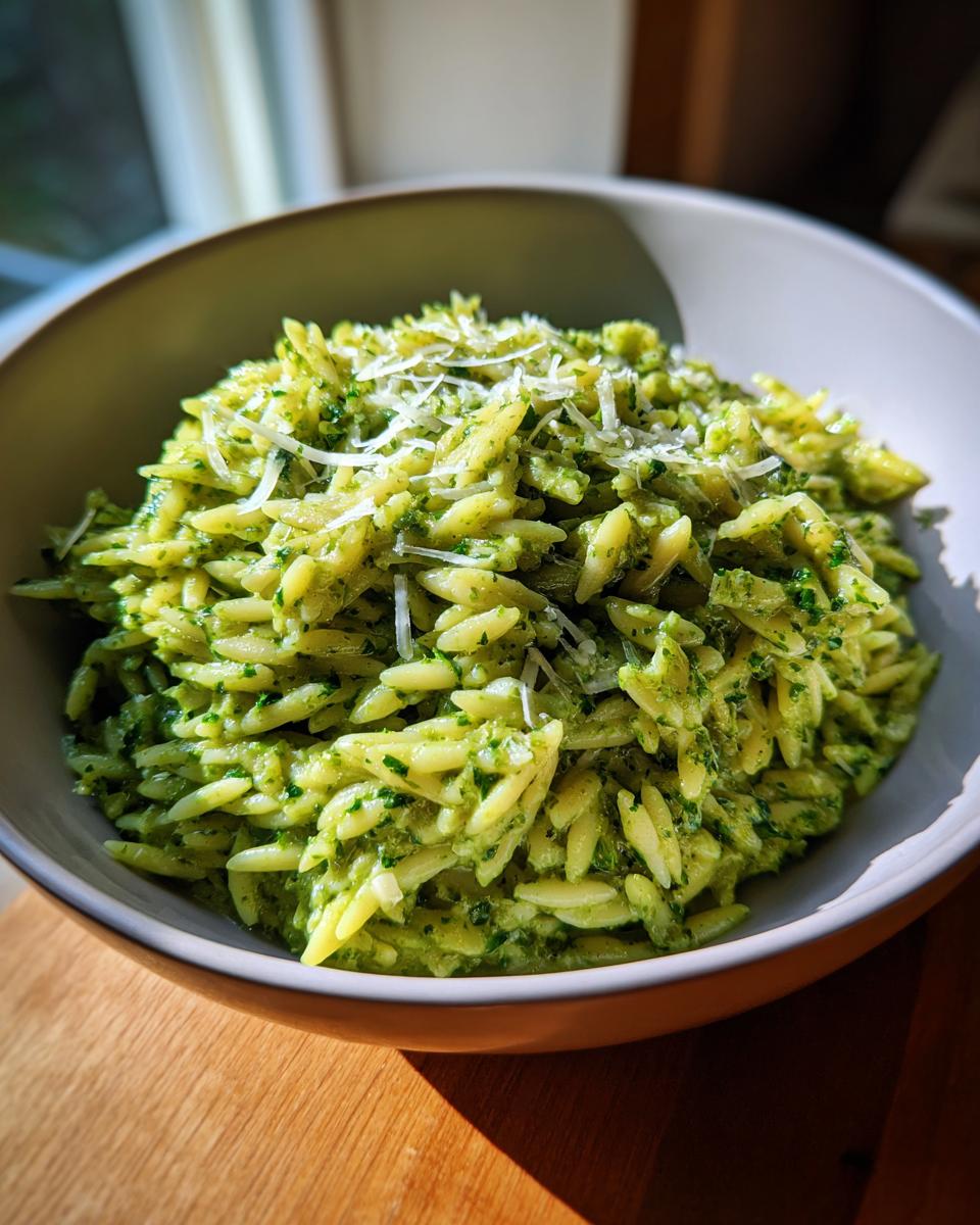 A bowl of bright green pesto orzo pasta, topped with grated parmesan cheese.
