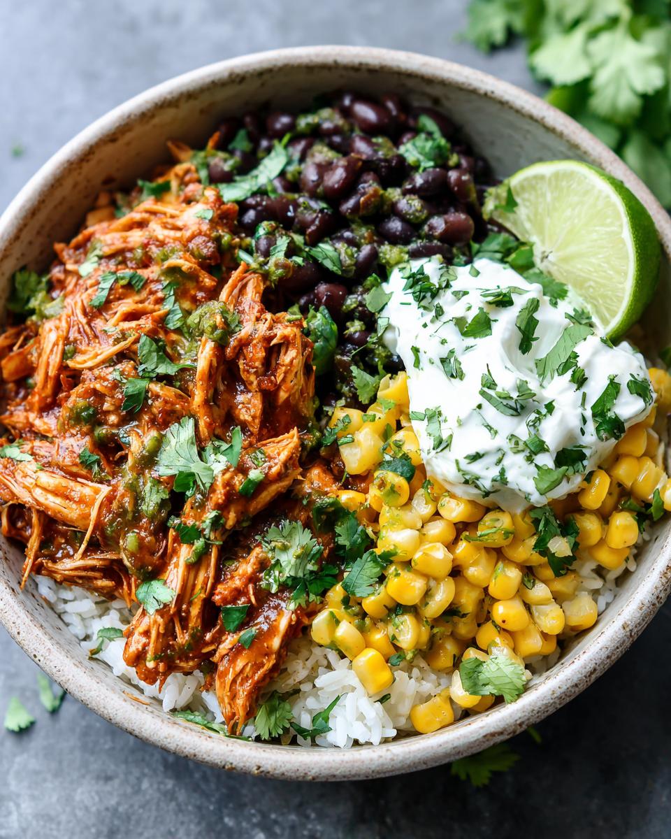 A delicious bowl of Salsa Verde Chicken Taco Bowl with shredded chicken, black beans, corn, rice, and sour cream.