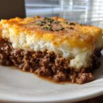 A close-up of a slice of Shepherd's Pie, showcasing the rich ground beef filling and creamy mashed potato topping.