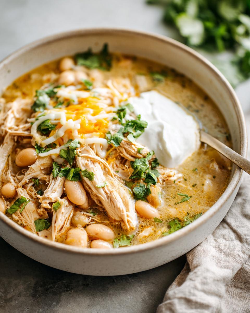 A bowl of flavorful Slow Cooker White Chicken Chili topped with shredded cheese, sour cream, and cilantro.