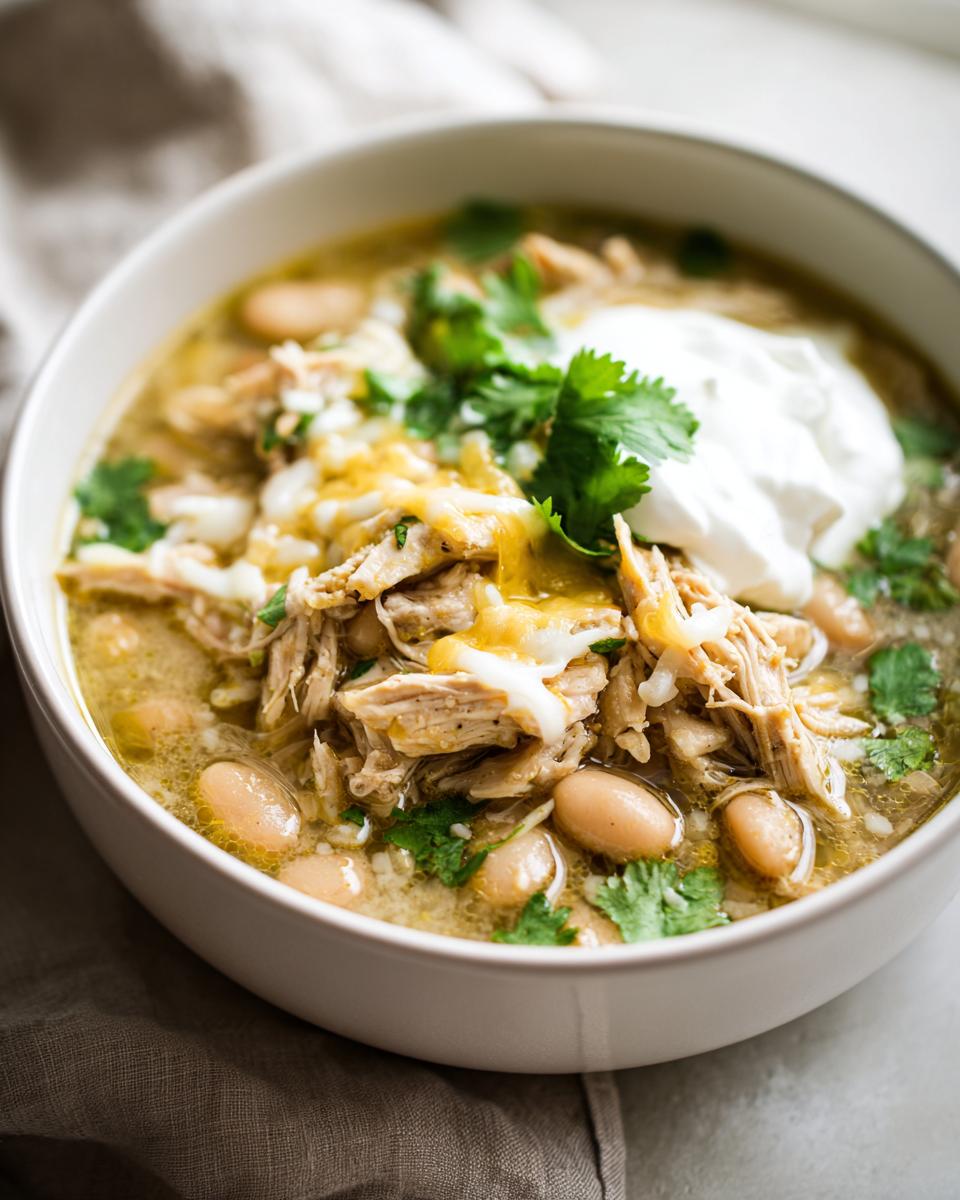 A bowl of delicious Slow Cooker White Chicken Chili, topped with cheese, sour cream, and cilantro.