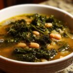 A close-up of a bowl of white bean kale soup, showcasing tender kale leaves and creamy white beans in a savory broth.